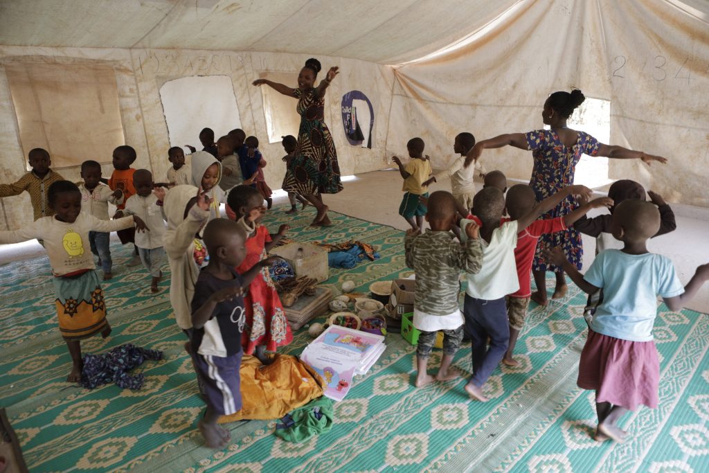 Two female teachers guide guide a group of children as they dance